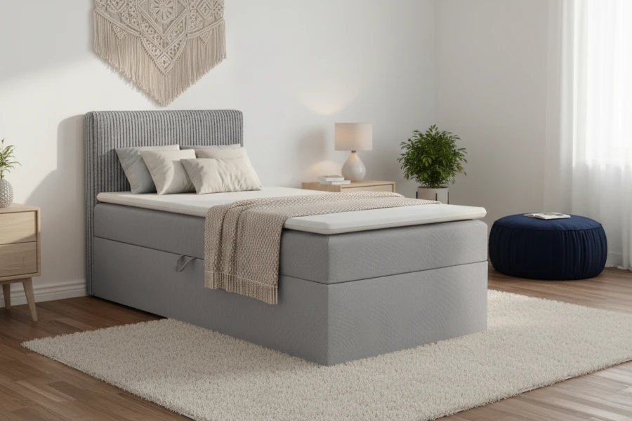 Graues Boxspring-Einzelbett im hellen Schlafzimmer mit Teppich und blauem Pouf.
