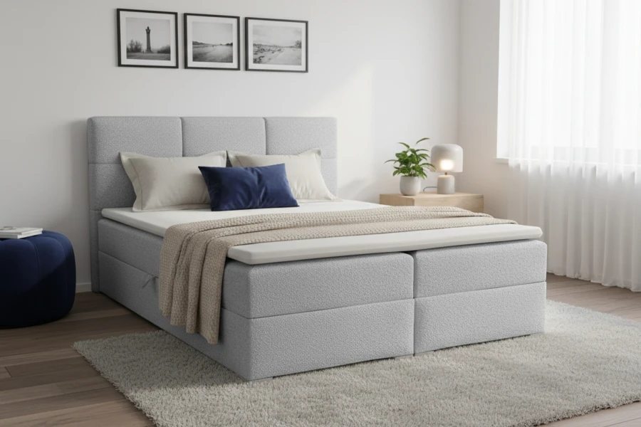 Hellgraues Boxspringbett im modern eingerichteten Schlafzimmer mit blauen Kissen und beiger Tagesdecke.