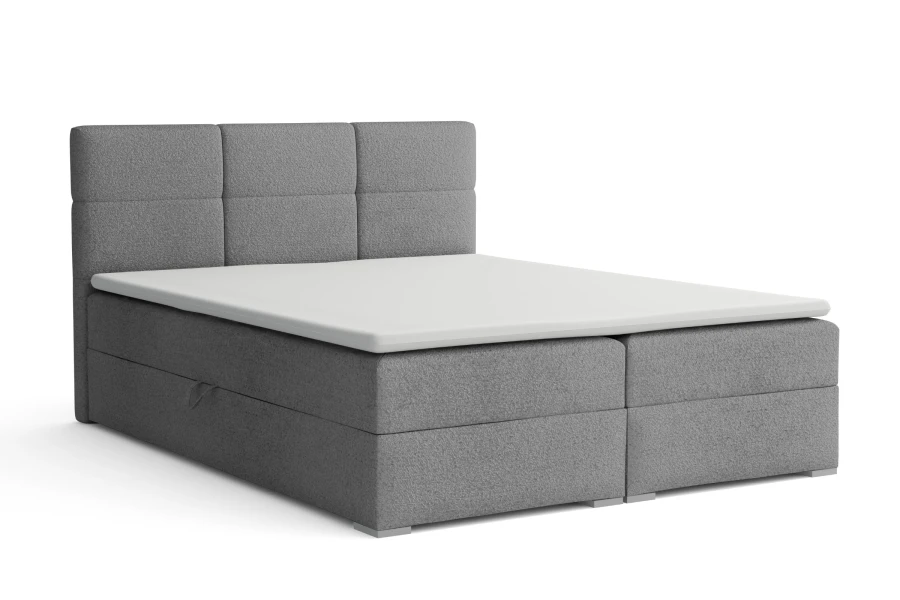Graues Boxspringbett mit hohem Kopfteil und weißer Topper-Auflage, freigestellt auf weiß.