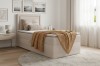 Cremefarbenes Boxspringbett mit Bettkasten und gelber Strickdecke in hellem Schlafzimmer.