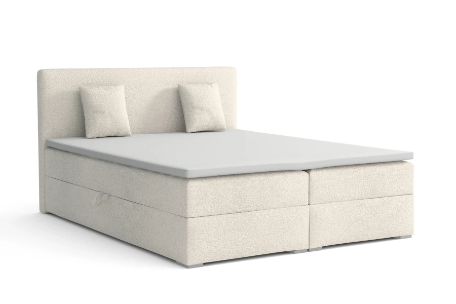Elegantes Boxspringbett in Creme mit gepolstertem Kopfteil und zwei Kissen vor weißem Hintergrund.