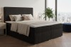 Schwarzes Cord-Boxspringbett mit gemütlichen Kissen und Stadtblick.