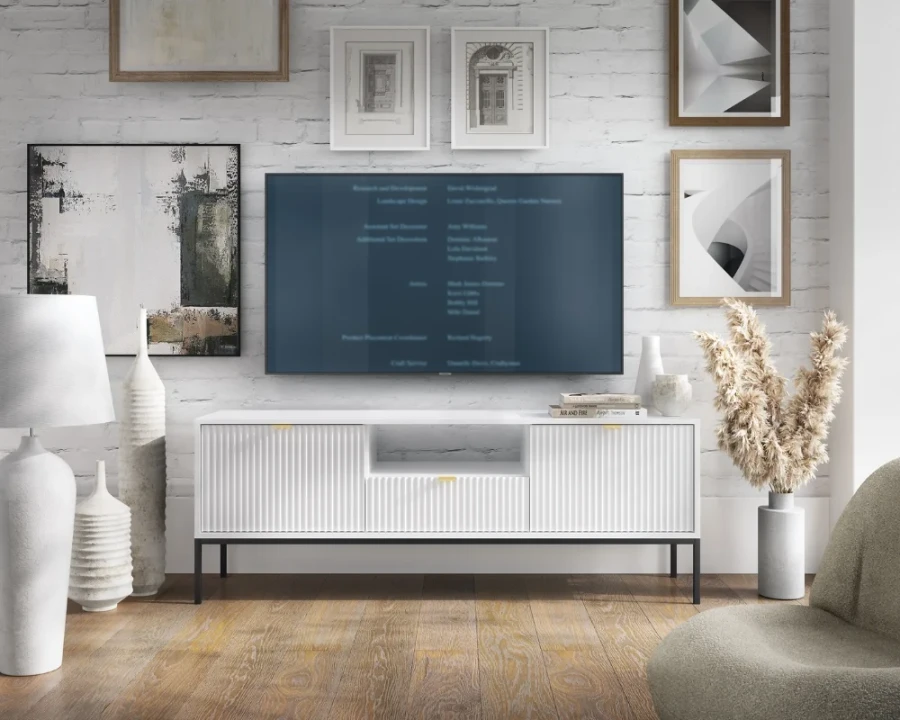 Weißes TV-Board mit Rillenstruktur im Wohnzimmer vor einer weißen Ziegelwand