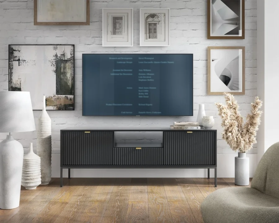 Eingerichtetes Wohnzimmer mit schwarzem TV-Board vor einer weißen Backsteinwand.