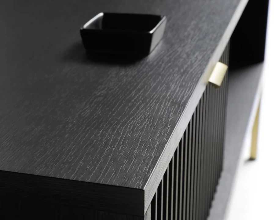Detailaufnahme der schwarzen Holzmaserung eines Sideboards mit goldenem Griff.