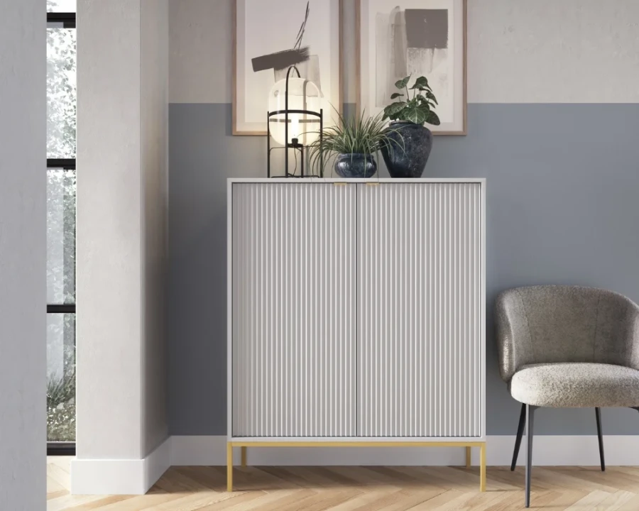 Moderner weißer Schrank mit Rillendesign und goldenen Metallbeinen vor blauer Wand.