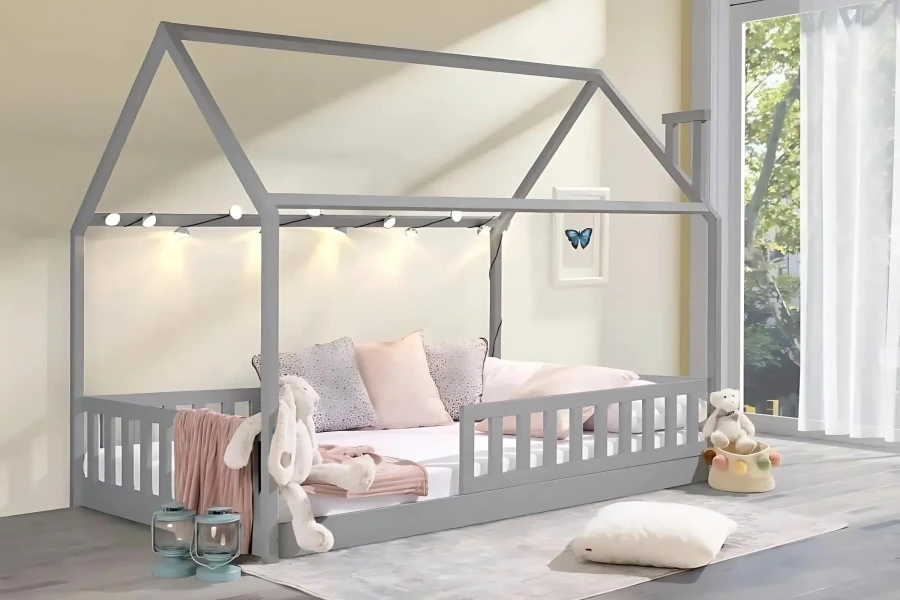 Gemütliches Kinderhausbett in Grau mit stimmungsvoller Lichterkette und rosa Kissen.