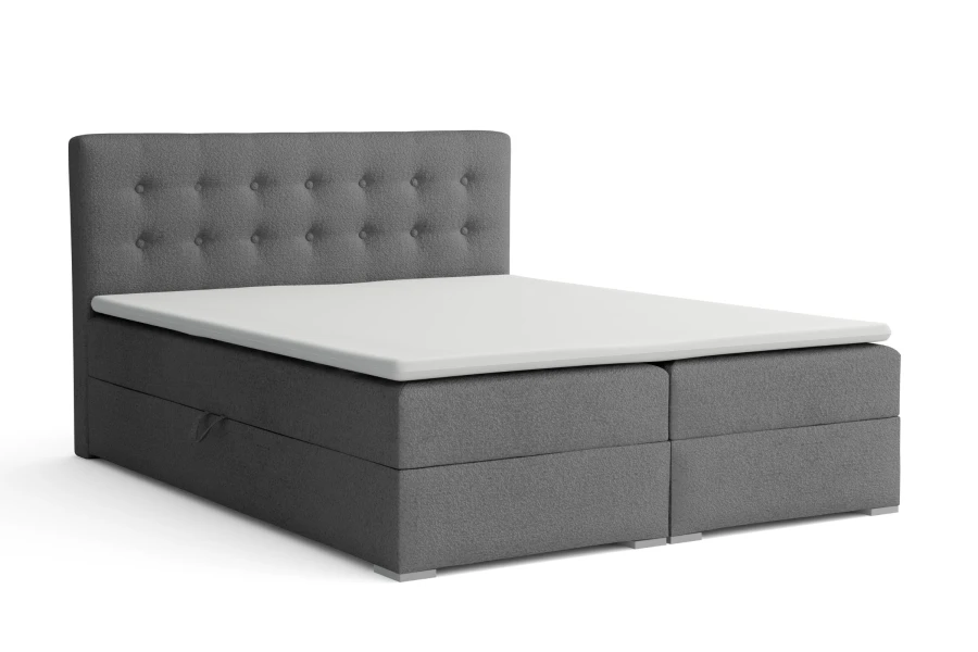 Graues Boxspringbett mit Knopfheftung am Kopfteil vor weißem Hintergrund.