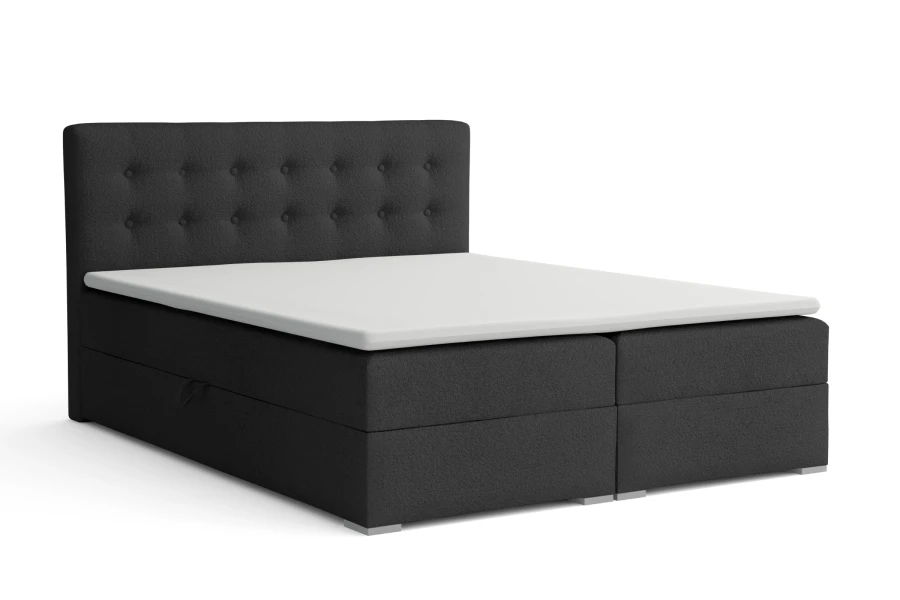 Dunkelgraues Boxspringbett mit gestepptem Kopfteil und weißem Topper auf weißem Hintergrund.
