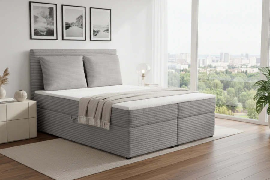 Graues Boxspringbett in Cord-Optik vor einem großen Fenster im modernen Schlafzimmer.