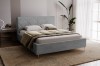 Graues Polsterbett im modern eingerichteten Schlafzimmer mit Teppich und Pflanze.
