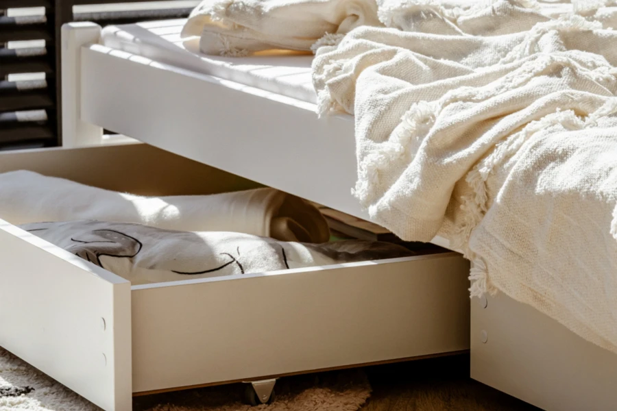 Ausziehbare Schublade unter einem weißen Kinderbett zur praktischen Aufbewahrung von Bettzeug.