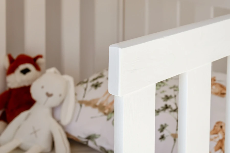 Weißes Holzkinderbett Detail mit Kuscheltieren im Hintergrund für eine gemütliche Atmosphäre.