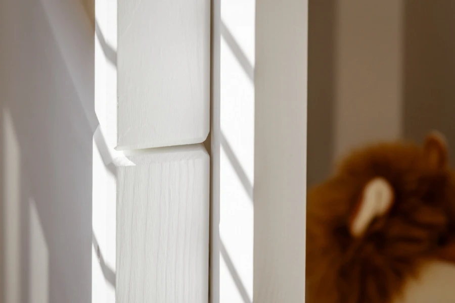 Detail eines weißen Bettpfostens aus Massivholz im hellen Kinderzimmer mit Schattenwurf.