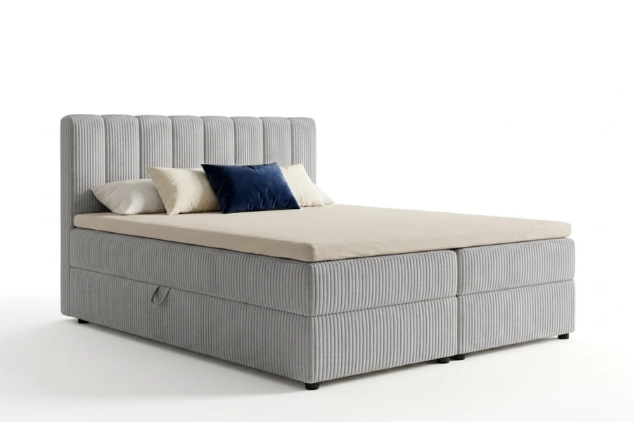 Graues Boxspringbett mit Cord-Stoff und Kissen freigestellt auf weißem Hintergrund.