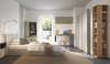 Helles Schlafzimmer mit salbeigrünen Schränken, Holzregal und gemütlichem Bettbereich.