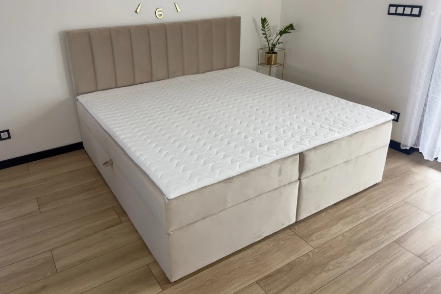 Seitenansicht eines beigen Polsterbettes mit Topper im modernen Schlafzimmer.