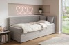 Helles Jugendzimmer mit grauem Cord-Tagesbett und rosa Herz-Neonleuchte an der Wand.