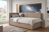 Moderne Eck-Boxspringliege in Beige mit Cord-Stoff und gemütlichen Kissen neben einem hellen Fenster.