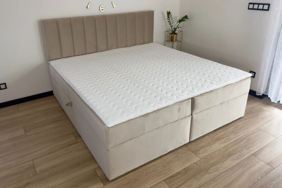Komplettes Boxspringbett VIKA in Beige mit weißem, gestepptem Topper in heller Umgebung.