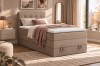 Beiges Boxspringbett im hellen Schlafzimmer mit Spiegel und dekorativen Kissen.
