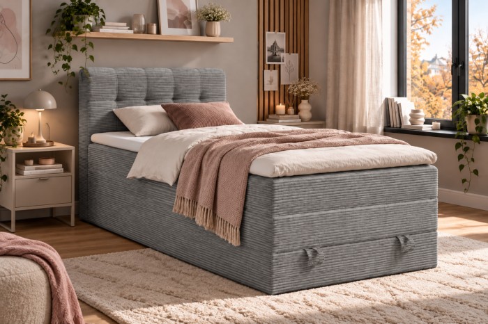 Hellgraues Boxspringbett aus Cord mit rosa Decke und grünen Pflanzen.