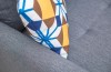 Geometrisches Dekokissen in Blau und Gelb auf einem grauen Polstersofa.