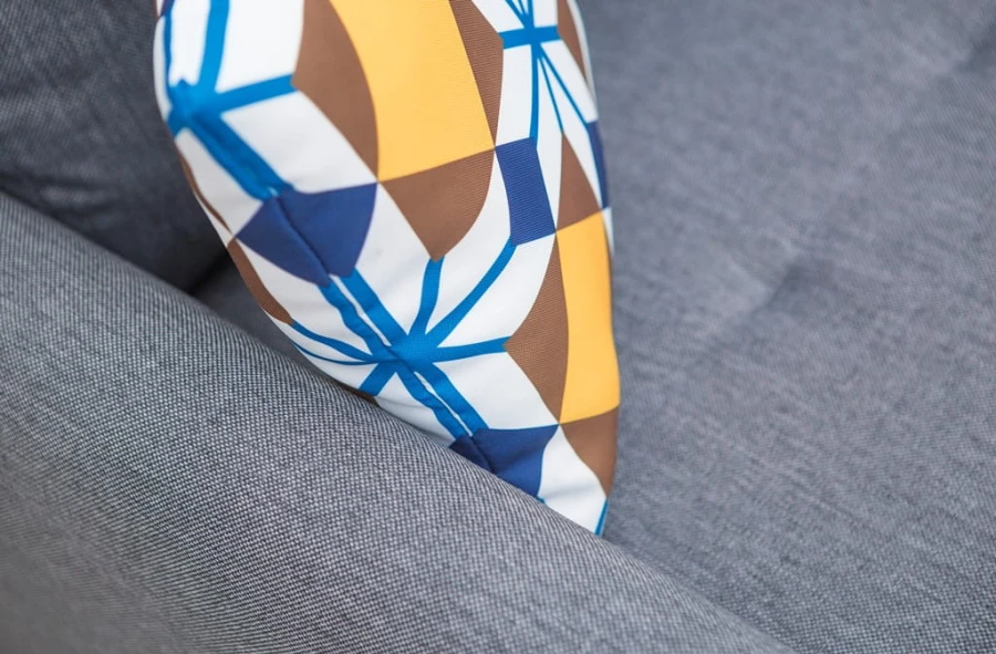 Geometrisches Dekokissen in Blau und Gelb auf einem grauen Polstersofa.